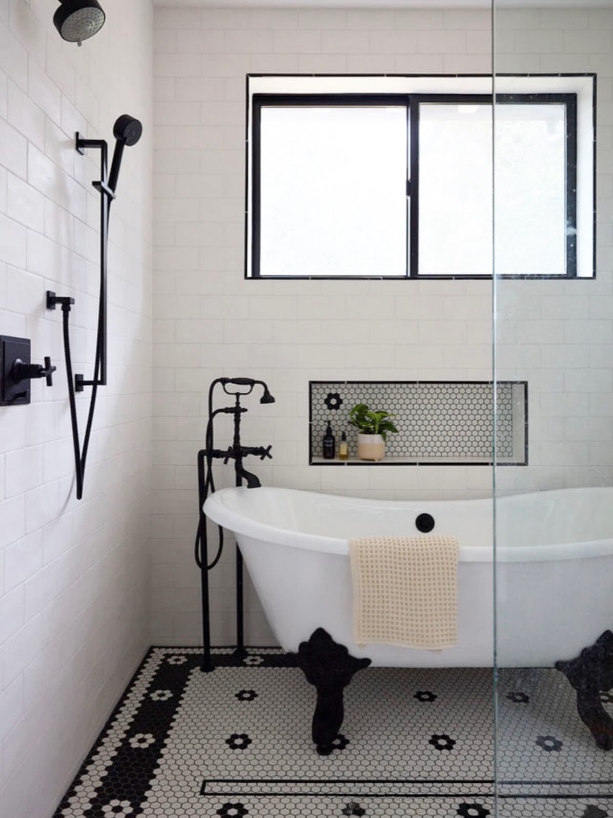 White clawfoot bathtub with black fixtures in a black and white tiled bathroom.