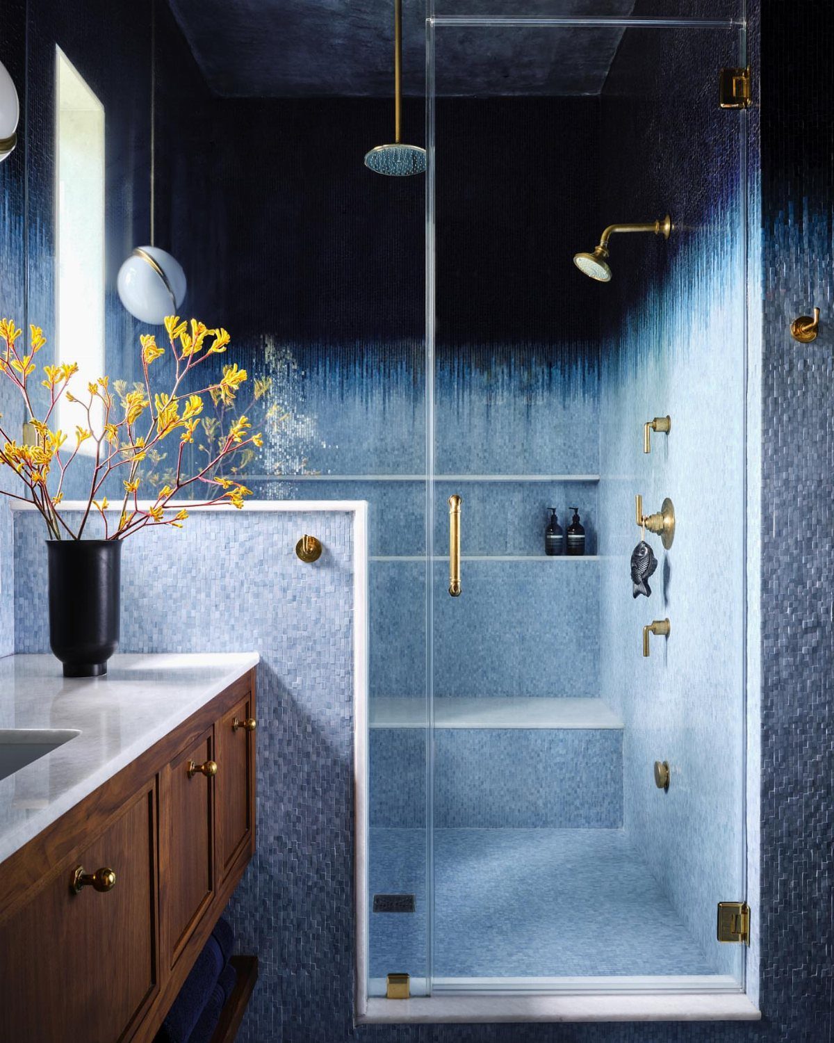 Glass shower enclosure with blue gradient textured tiles and gold hardware in bathroom