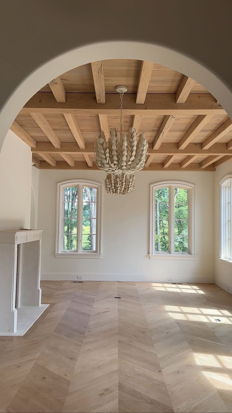 Empty room with herringbone wood floors, beamed ceiling, and a large textured chandelier.