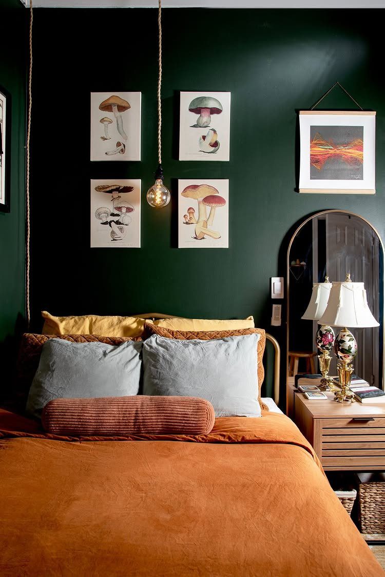 Bedroom with dark green walls, orange bedding, and mushroom art prints above bed.