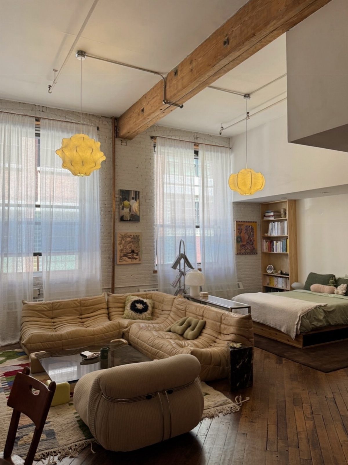 Open concept loft with exposed beams, tan modular sofa, and yellow pendant lights.