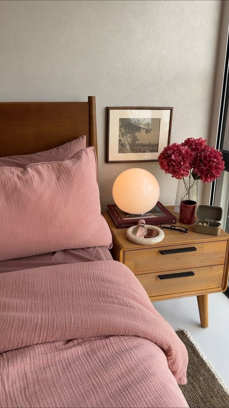 Pink bed linens and a wooden nightstand with a glowing orb lamp.