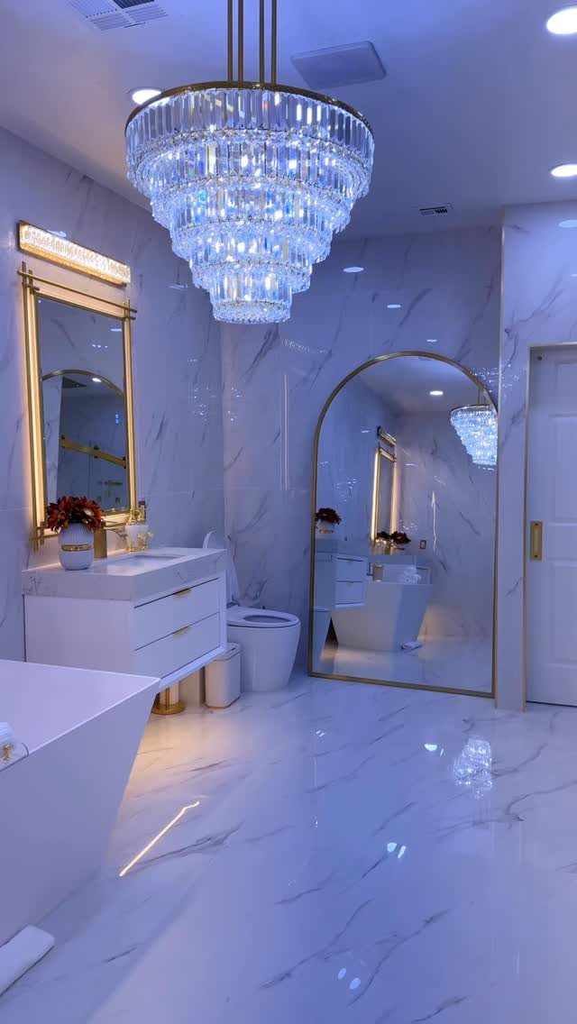 Luxurious white marble bathroom with a crystal chandelier and gold accents.