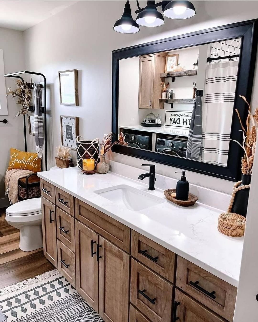 Wooden bathroom vanity with white countertop and large black-framed mirror in farmhouse style.