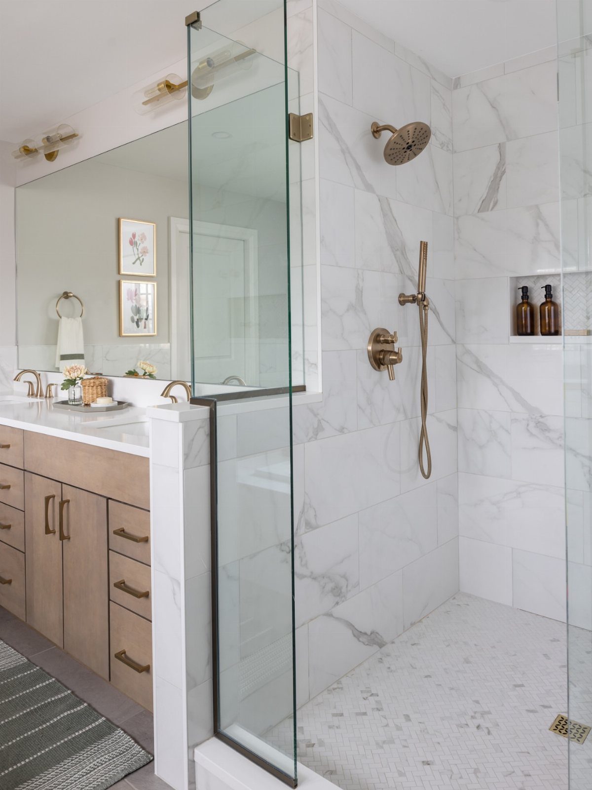 Frameless glass shower enclosure in a white marble bathroom with gold fixtures.