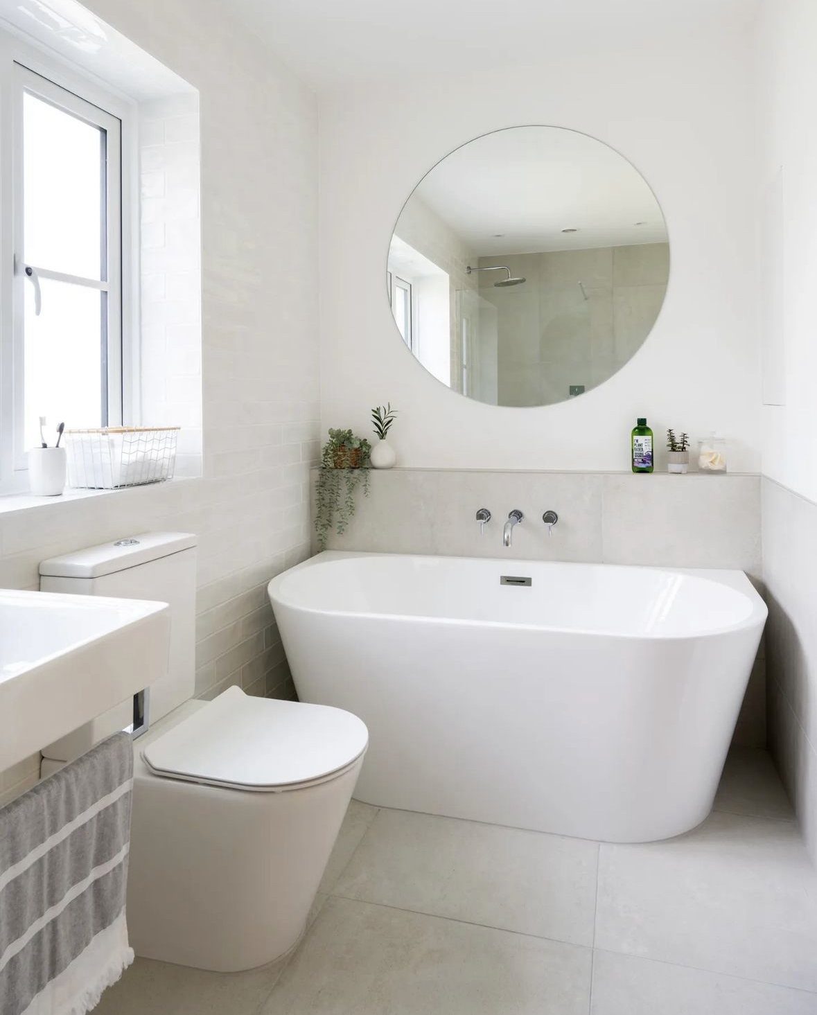 White freestanding bathtub in a bright white bathroom with a circular mirror.