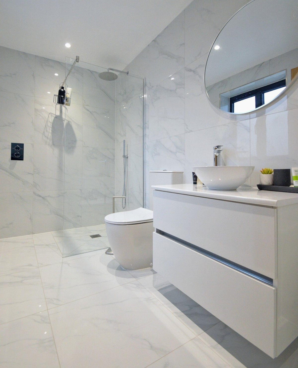 Modern white bathroom with marble tiles, floating vanity, and frameless glass shower.