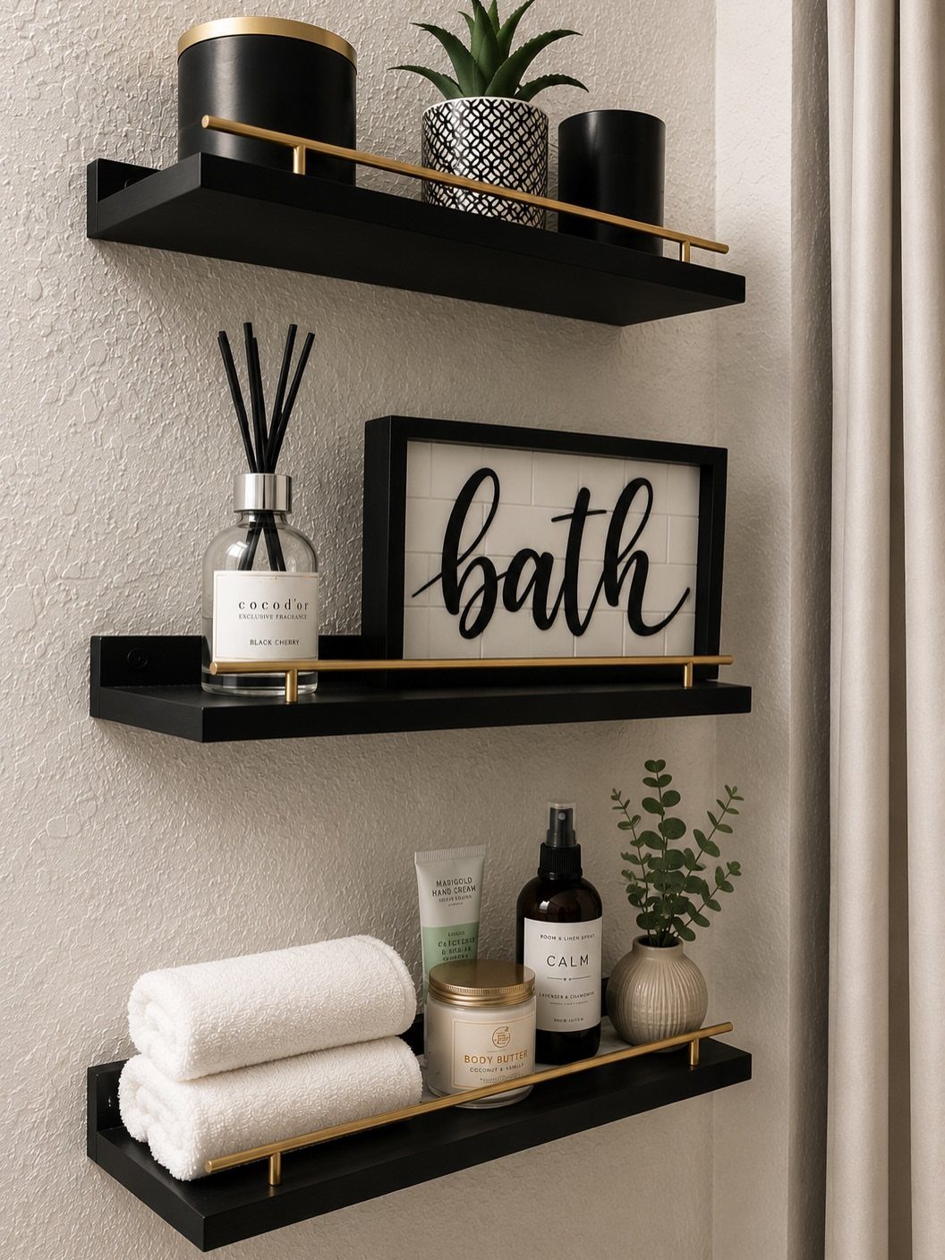 Black floating shelves with gold rails holding bathroom accessories on a white wall.
