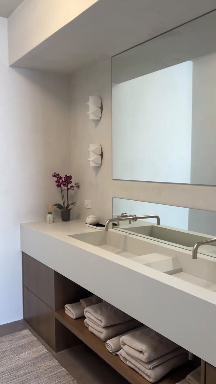 White bathroom vanity with a large mirror and beige towels on open shelving.