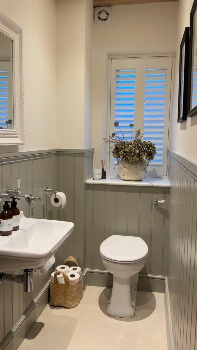 Grey vertical wall paneling in a small bathroom with white fixtures and shutters.