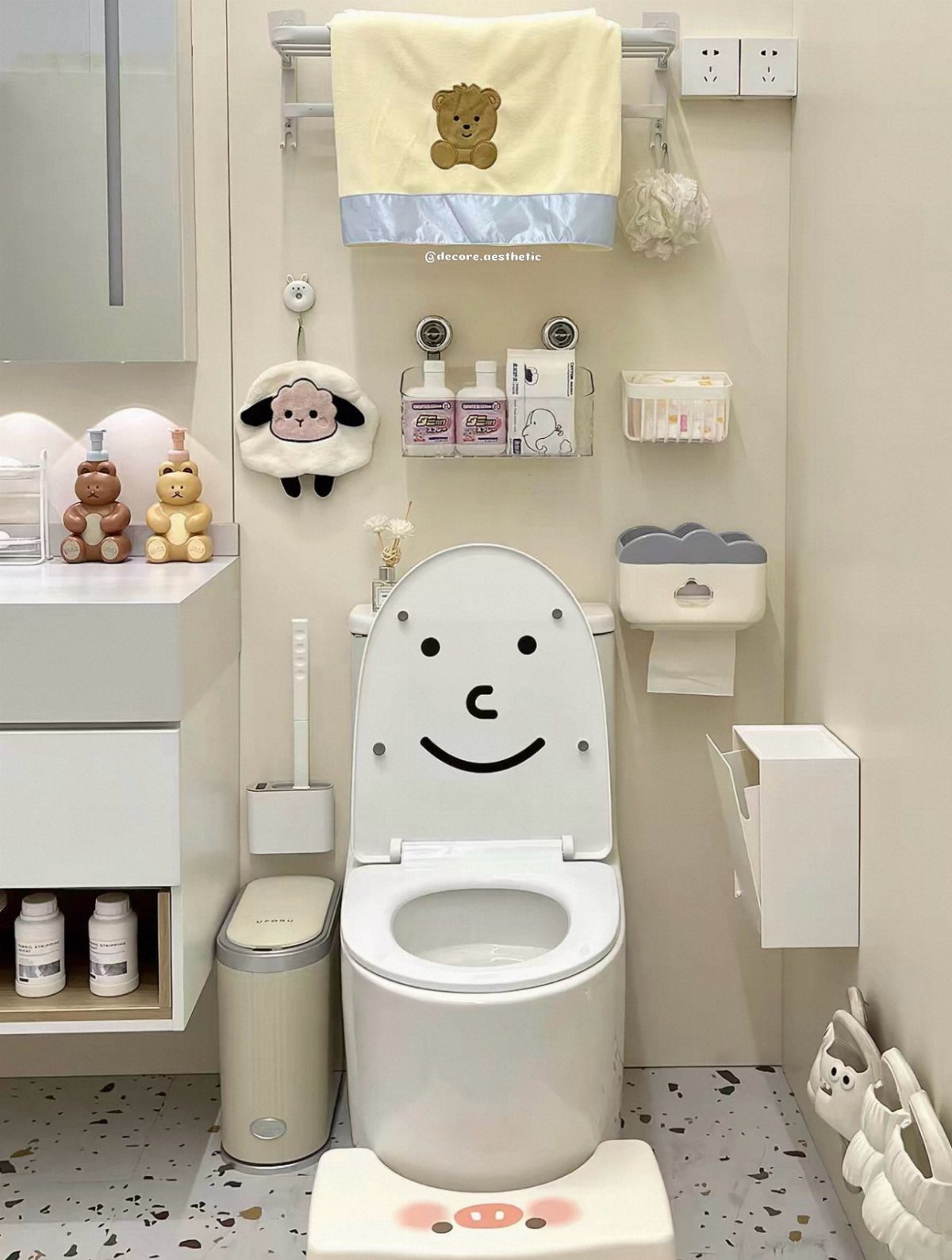 White bathroom with a smiling toilet lid, pig mat, and cute bear towel.