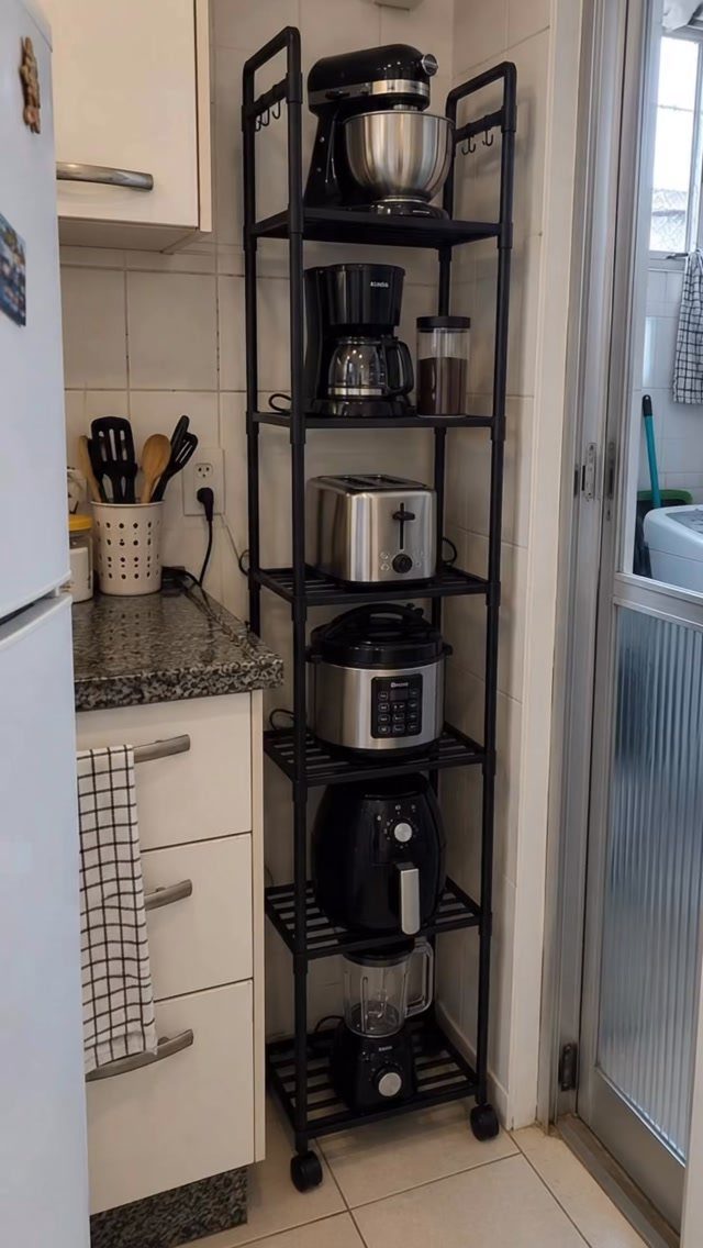 Black metal vertical shelving unit holding various kitchen appliances in a small kitchen.