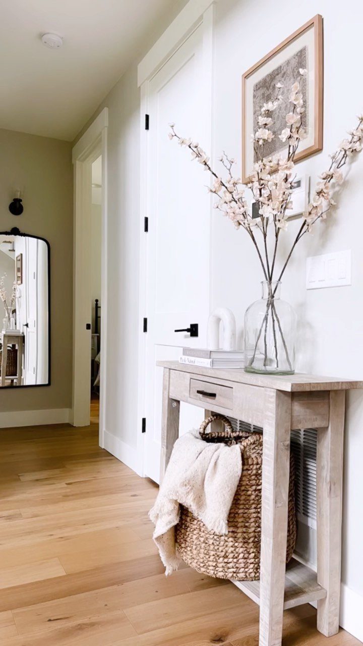 Slim light-wood console table with a vase of flowers and woven storage basket.