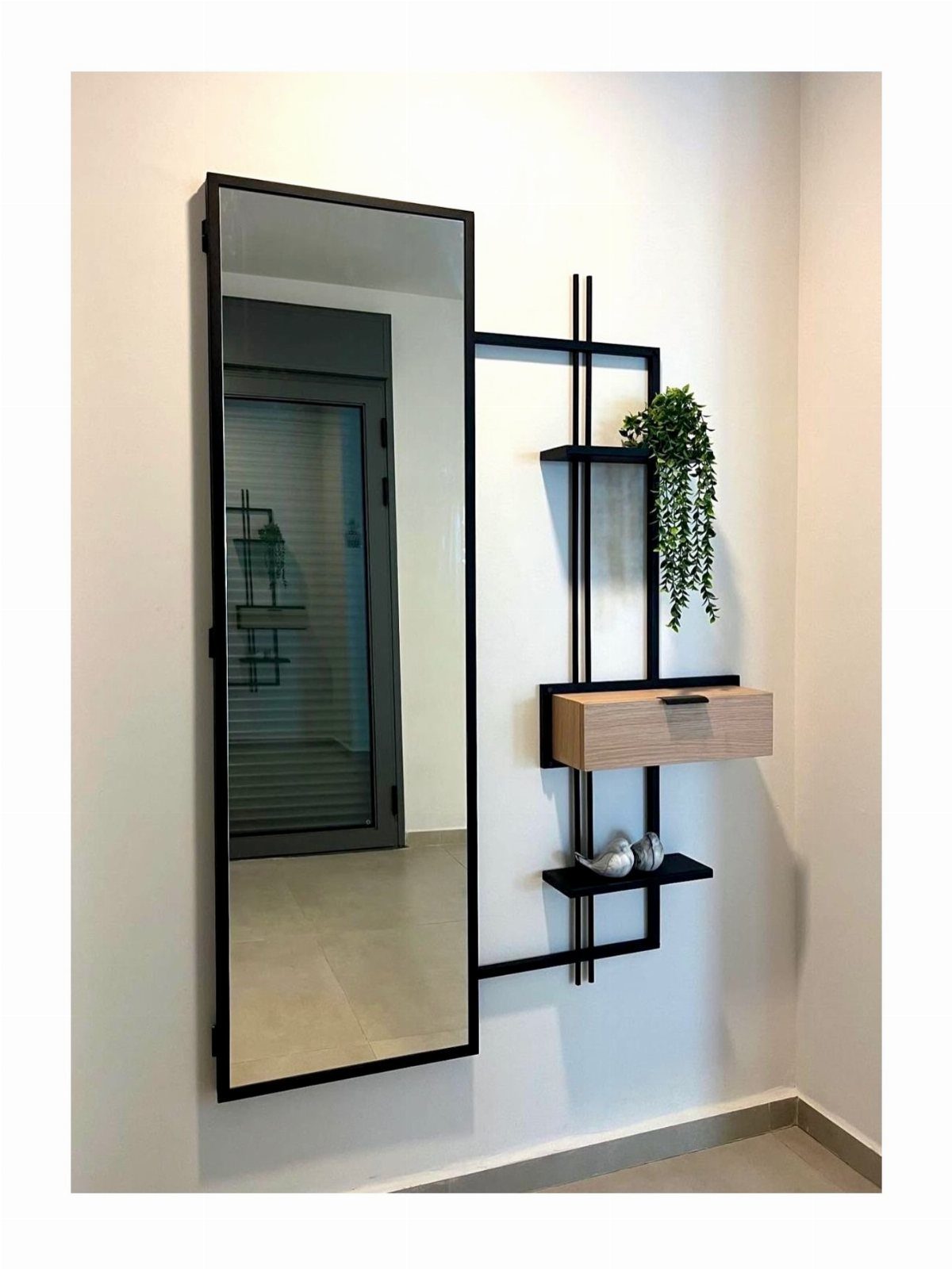 Tall black framed mirror and matching wall shelf with a small plant.