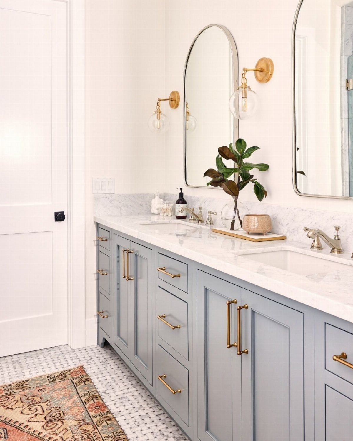 Light blue-grey bathroom vanity with gold hardware and white marble countertops.