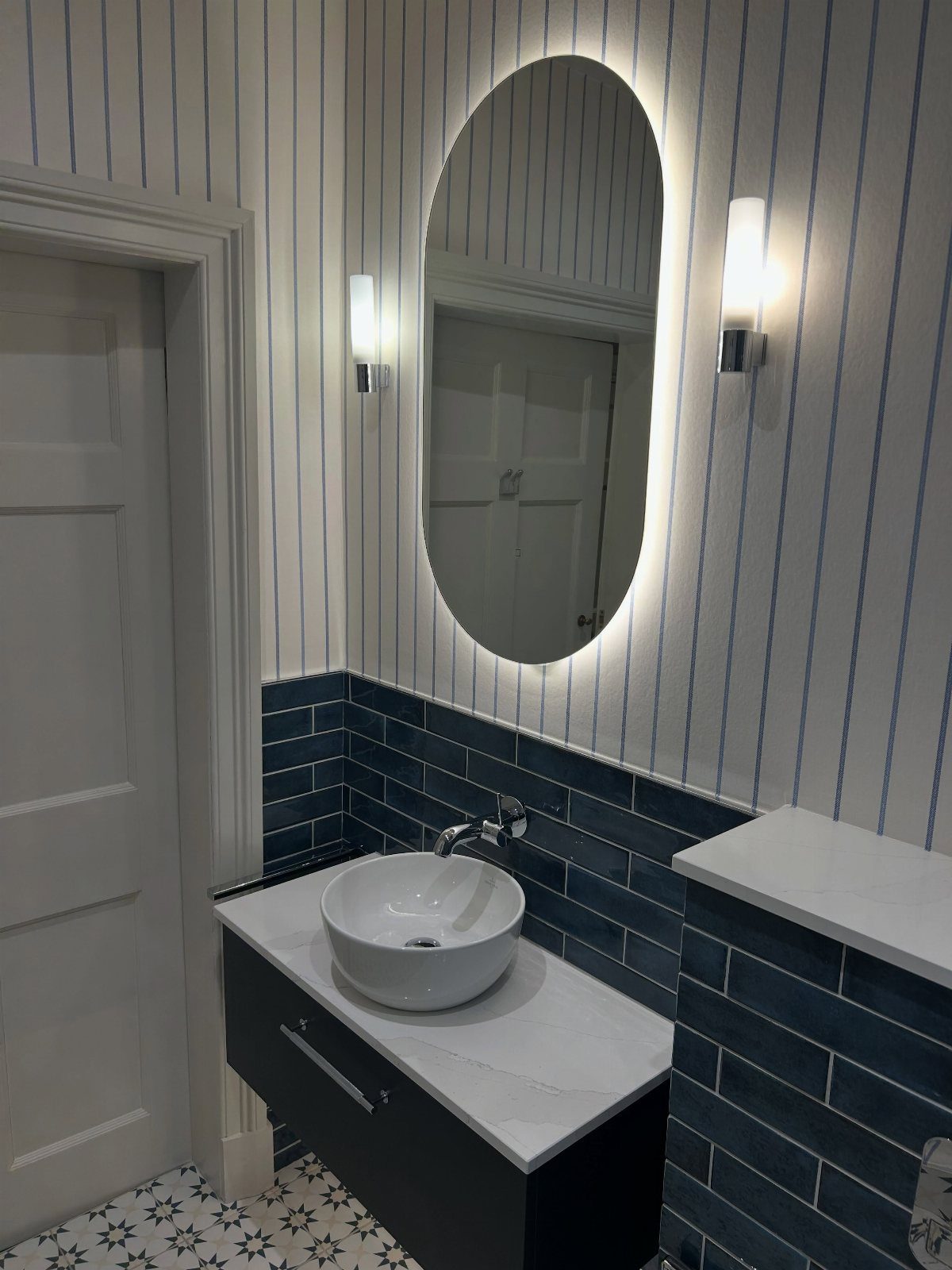 Blue and white striped wallpaper in a bathroom with navy subway tile backsplash.