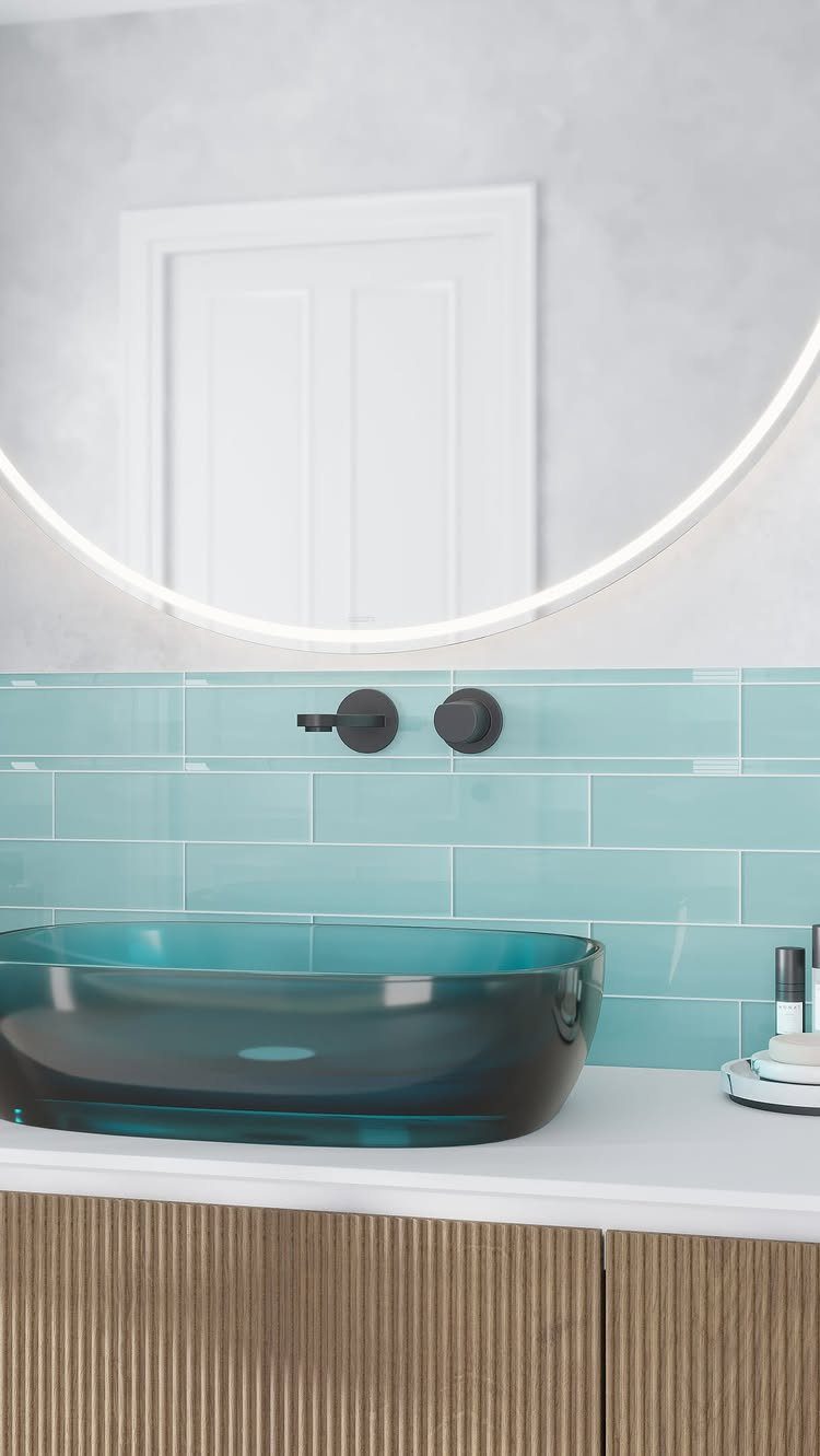 Blue glass vessel sink with light blue subway tile backsplash and backlit mirror.