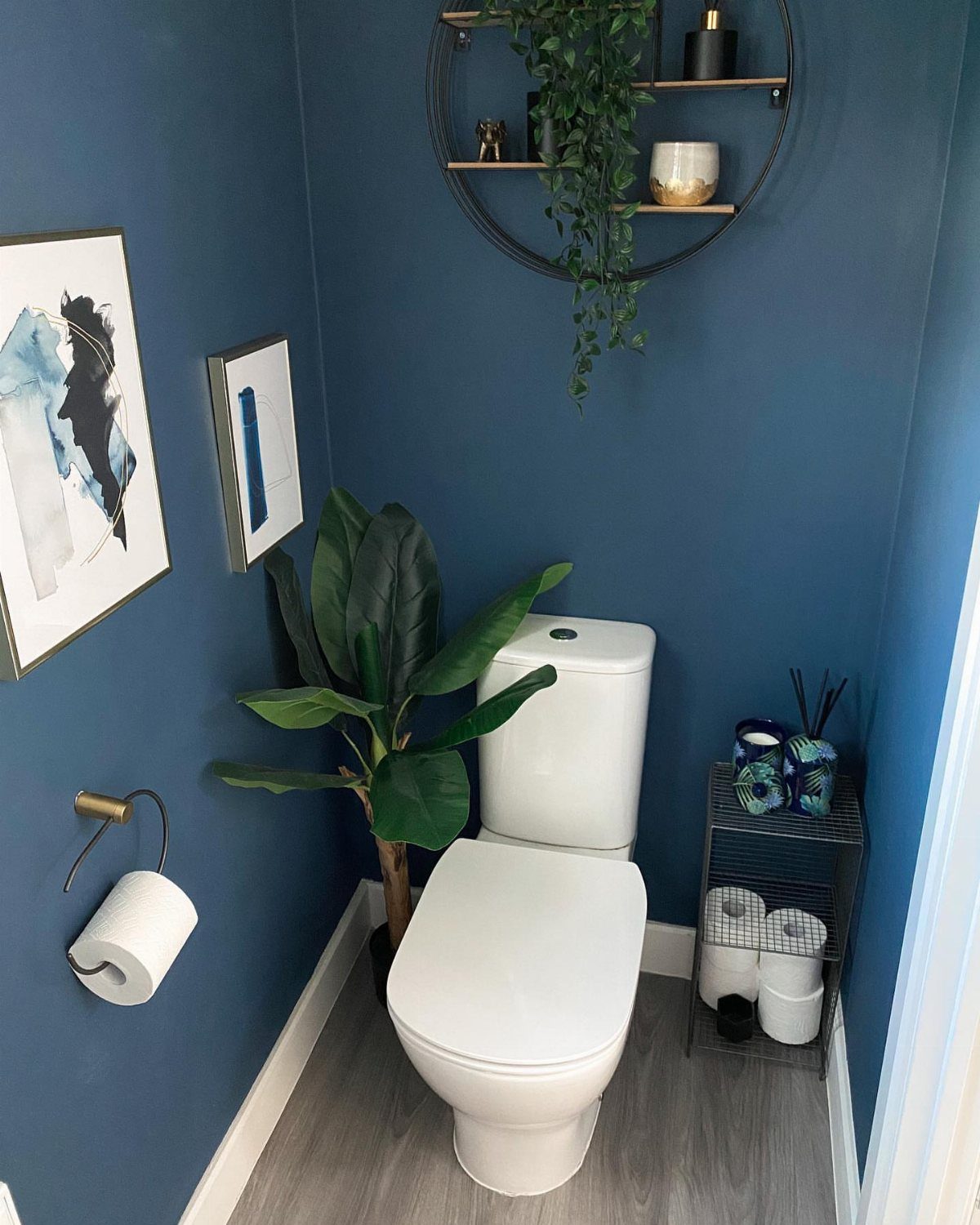 Deep blue bathroom walls with a white toilet and gold accents.