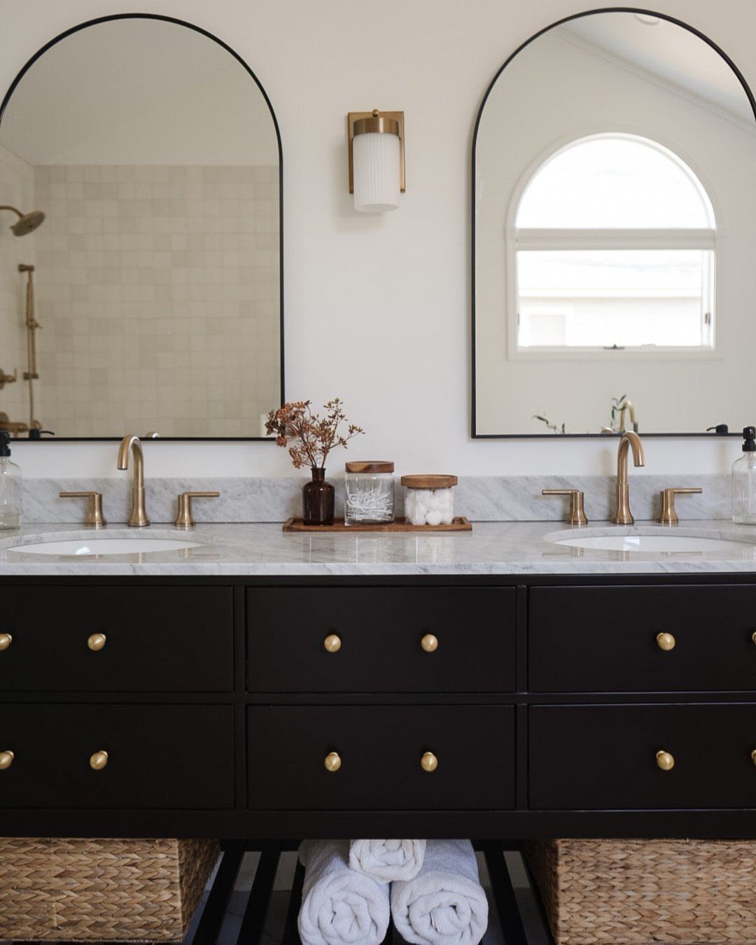 Black double sink bathroom vanity with marble top and arched black mirrors.
