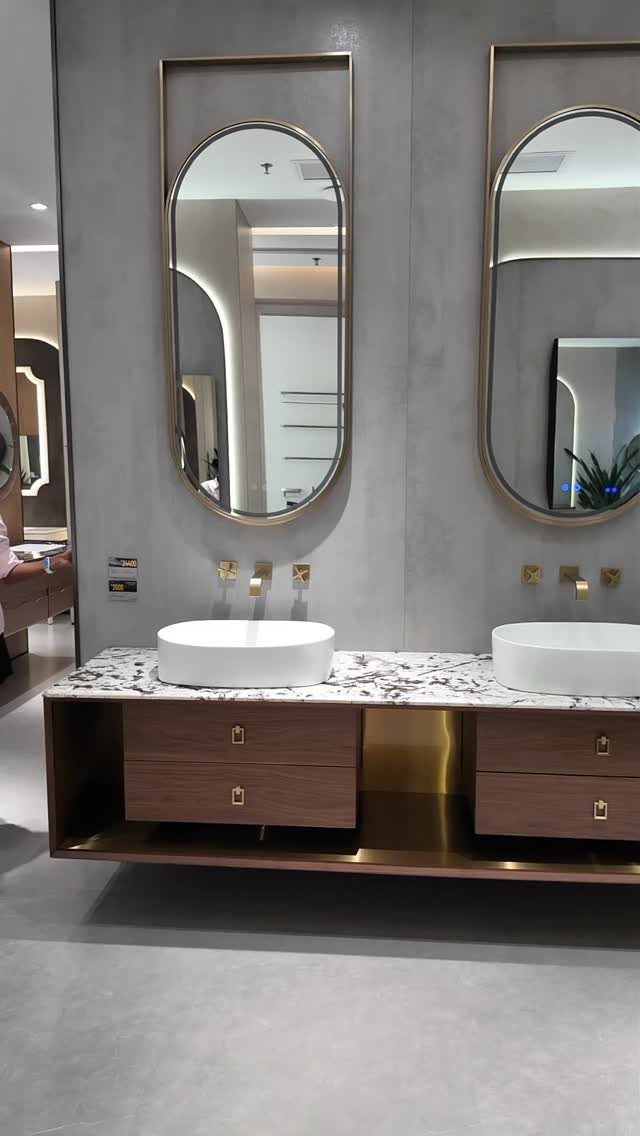 Double sink bathroom vanity with marble top, wooden drawers, and gold-framed oval mirrors.