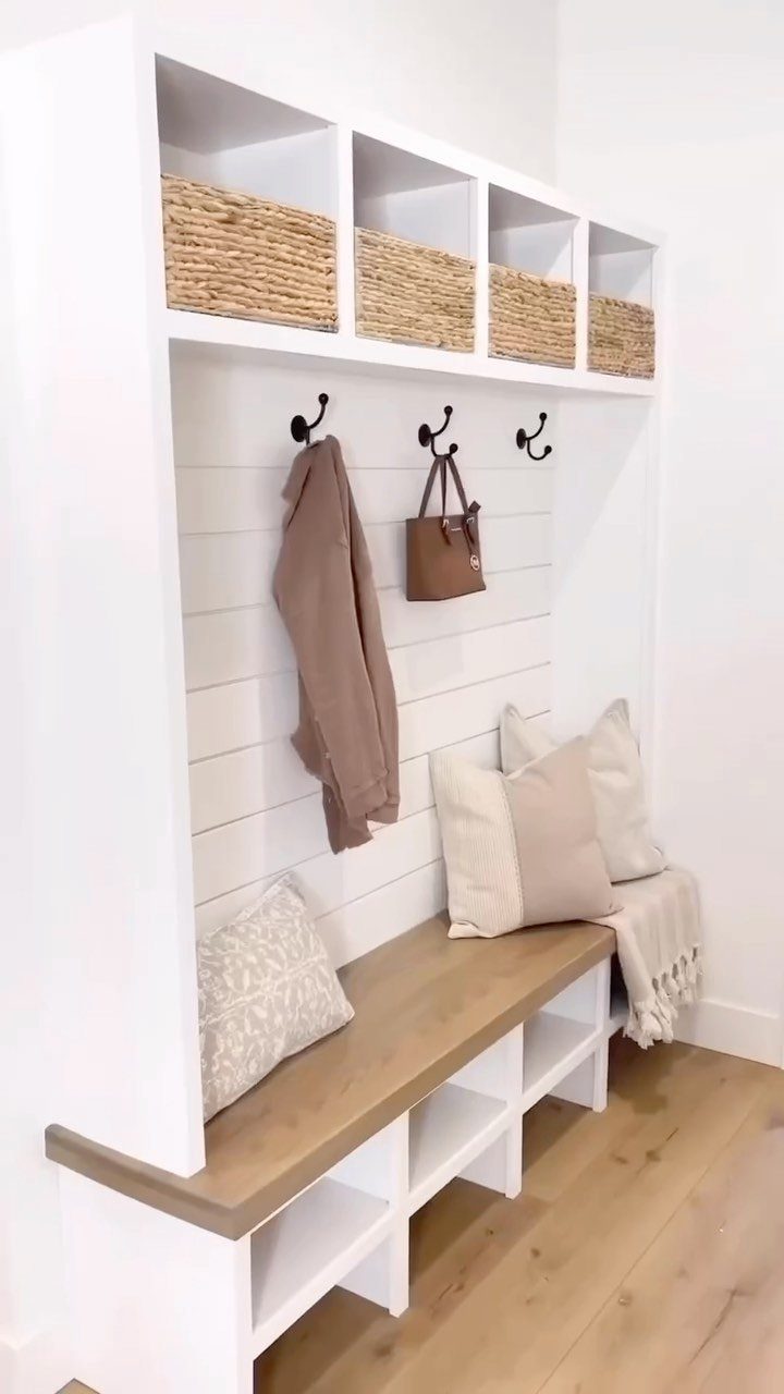 White built-in mudroom unit with woven baskets, hooks, and a wooden bench.