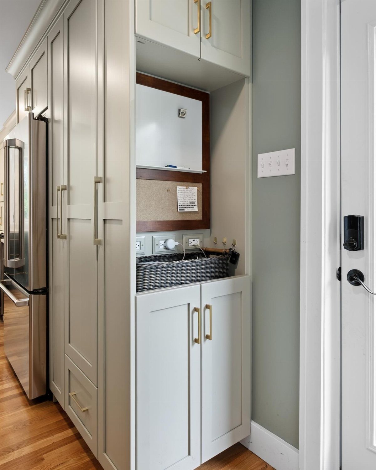 Built-in white cabinet nook with a woven catch-all tray and corkboard by a door.