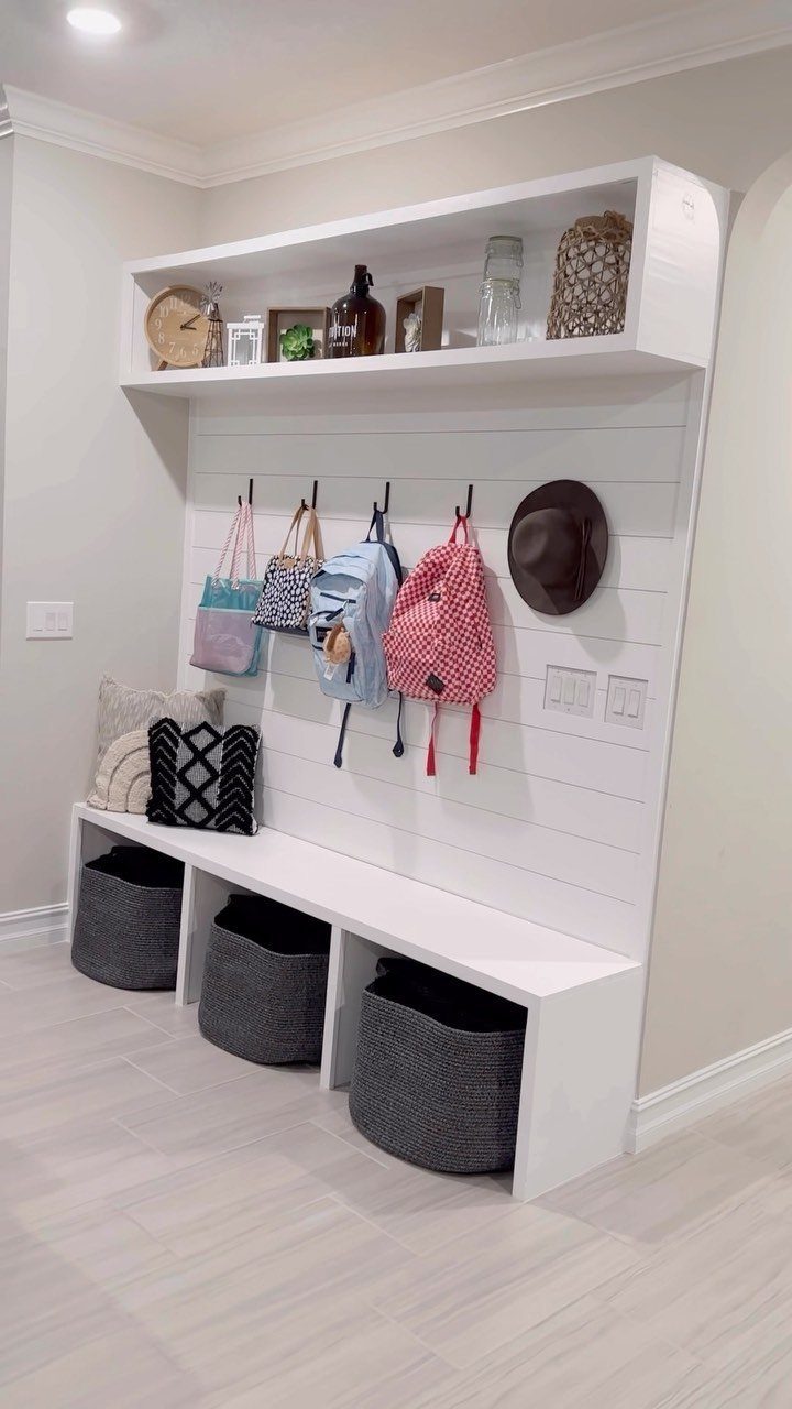 White entryway organizer with a bench, cubbies with baskets, and hooks for bags.