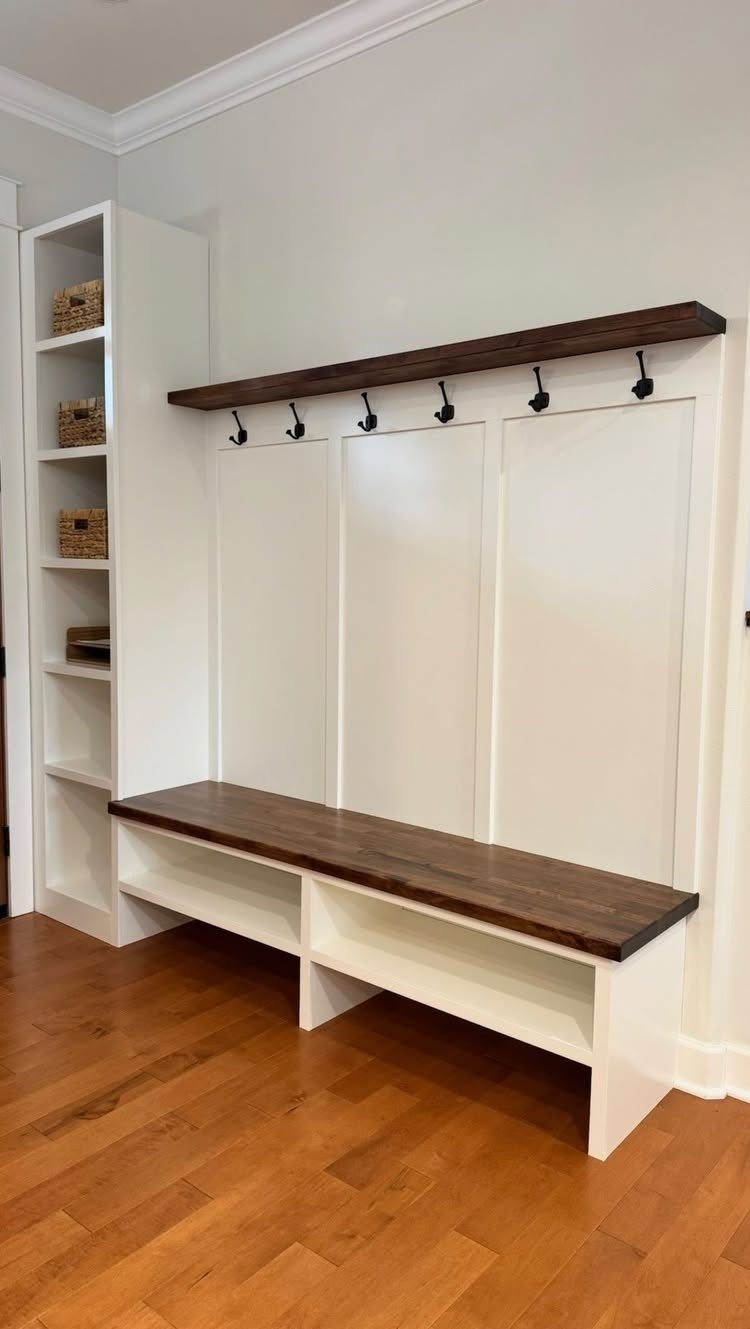 White built-in entryway unit with dark wood bench, hooks, and side shelving.