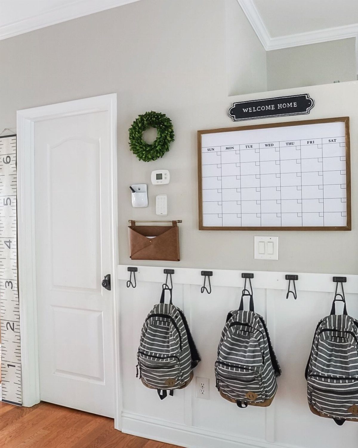 Three striped backpacks hanging from black hooks on a white wainscoted wall.