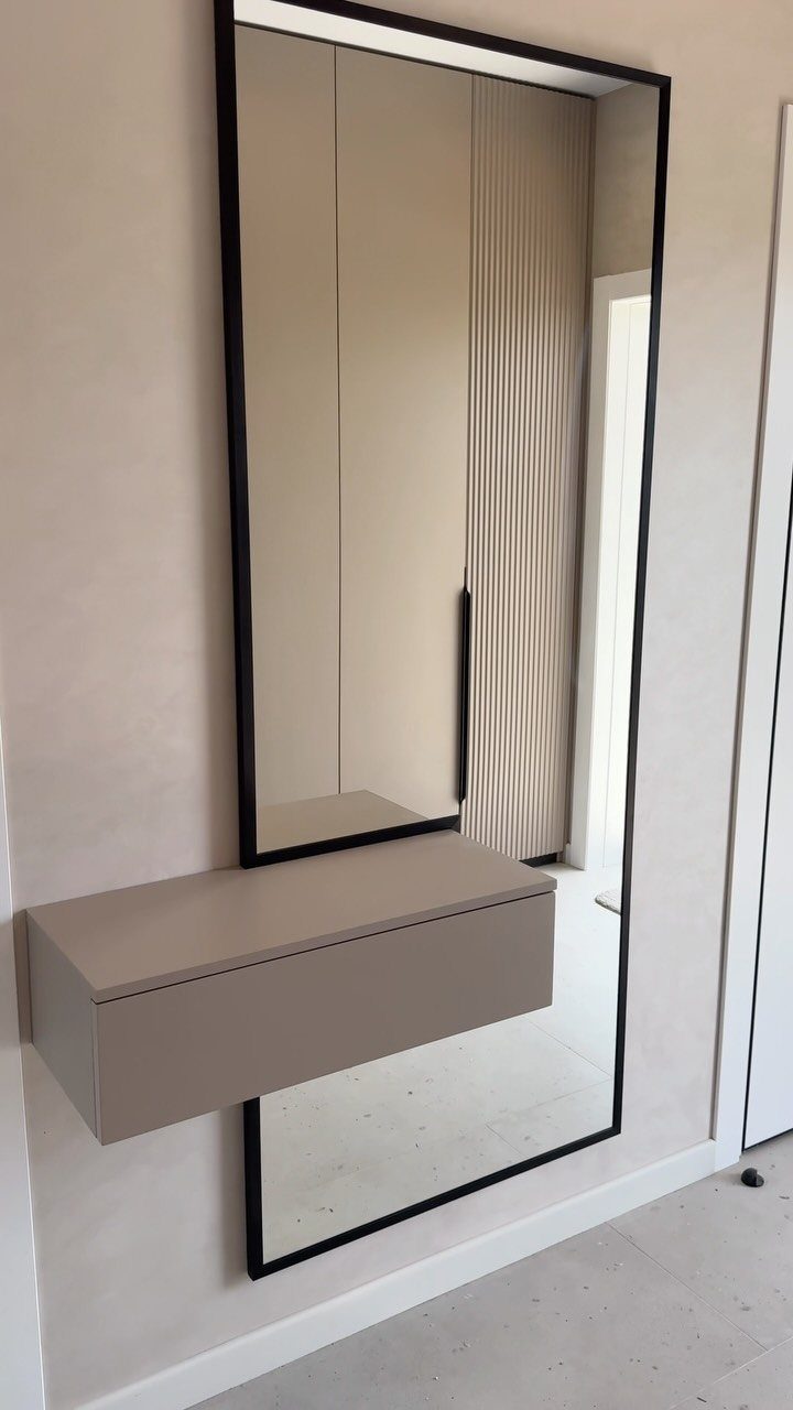 Tall black-framed mirror with a floating beige shelf in a minimalist hallway.