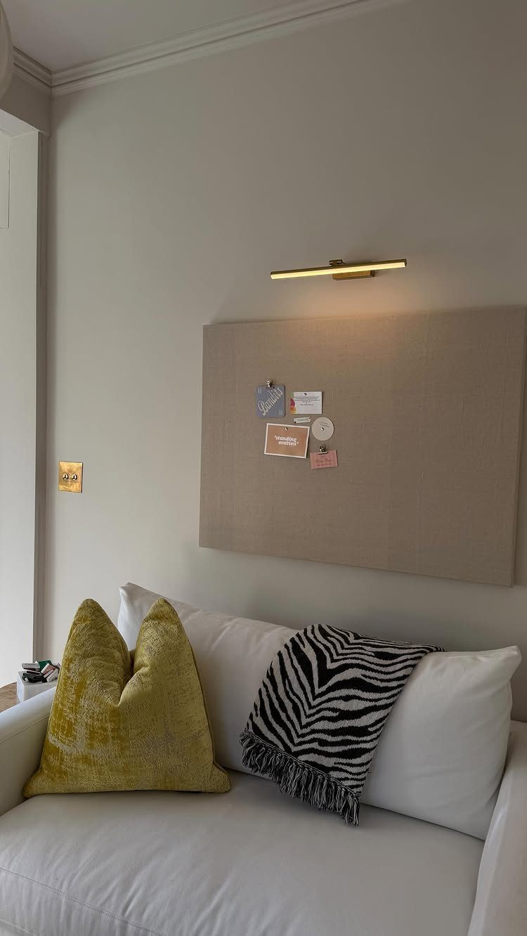 Beige fabric pin board with notes mounted on a wall above a white sofa.