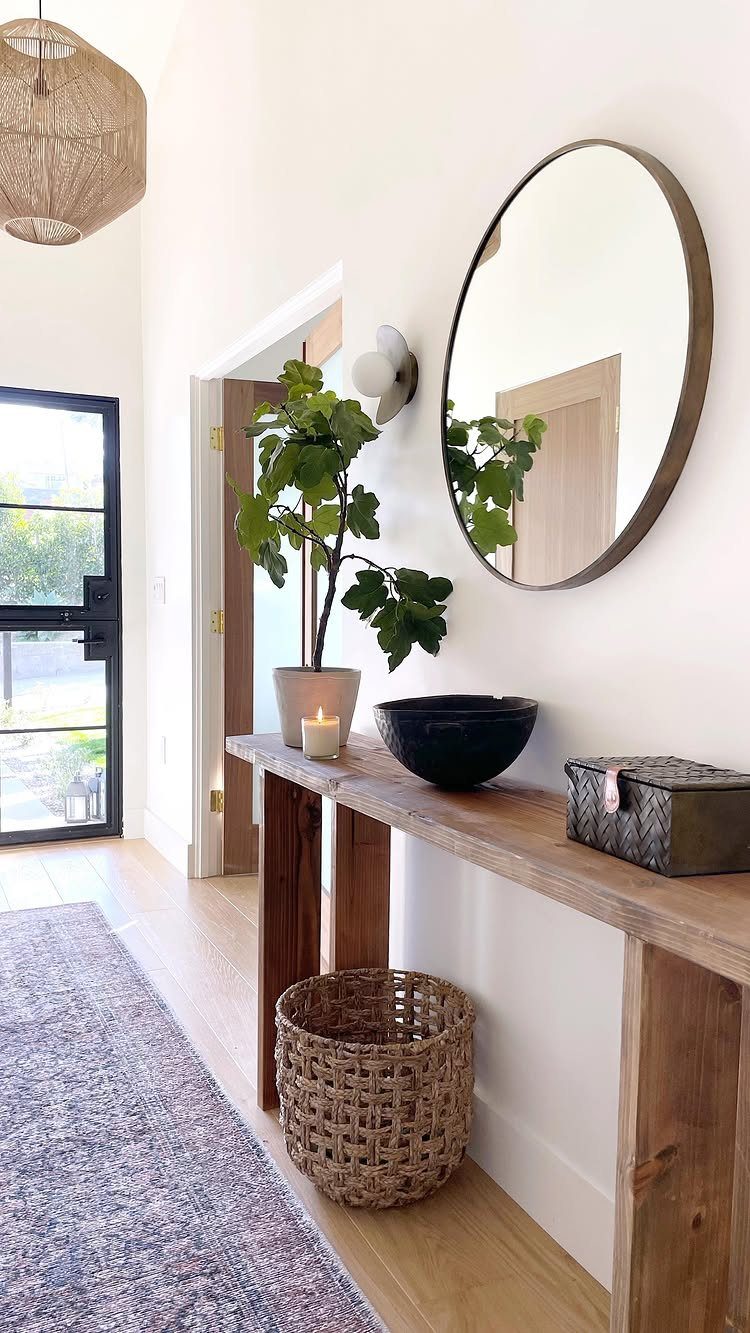 Slim wooden console table with a round mirror and woven basket in entryway