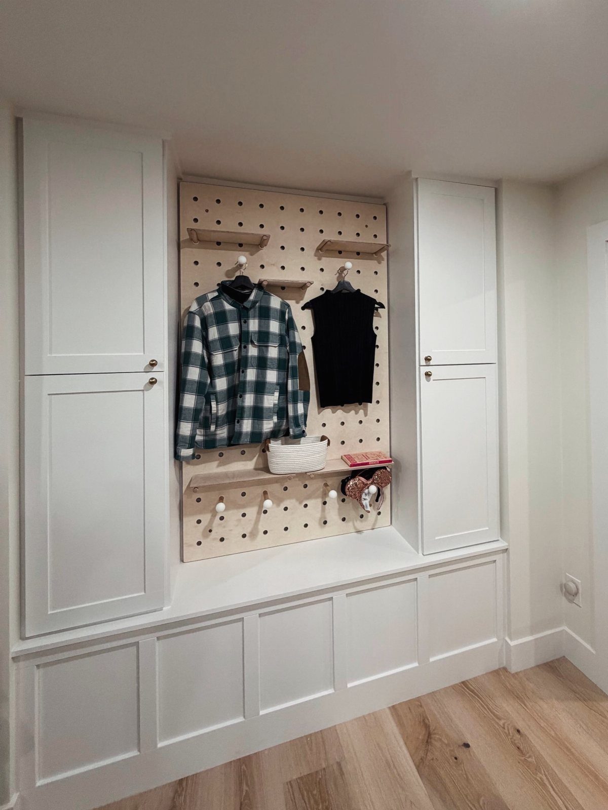 White built-in mudroom with a central pegboard, storage cabinets, and a long bench.
