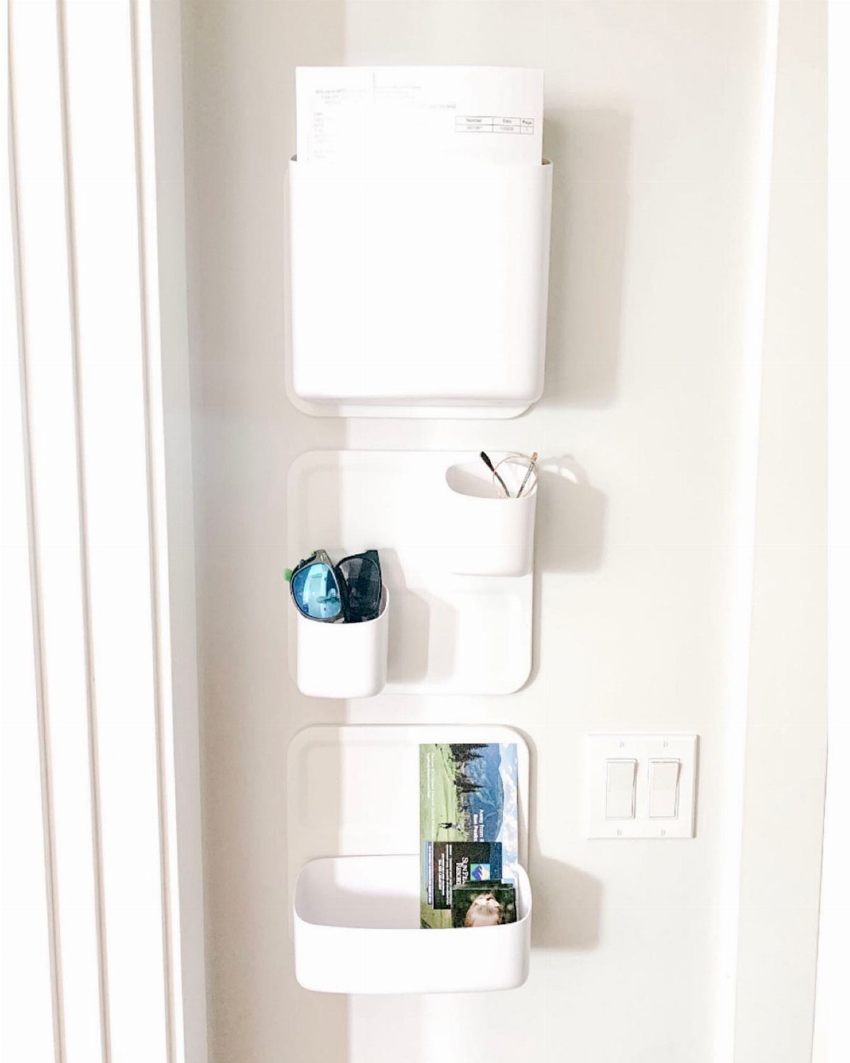 White wall-mounted mail and document holders containing papers and a magazine.