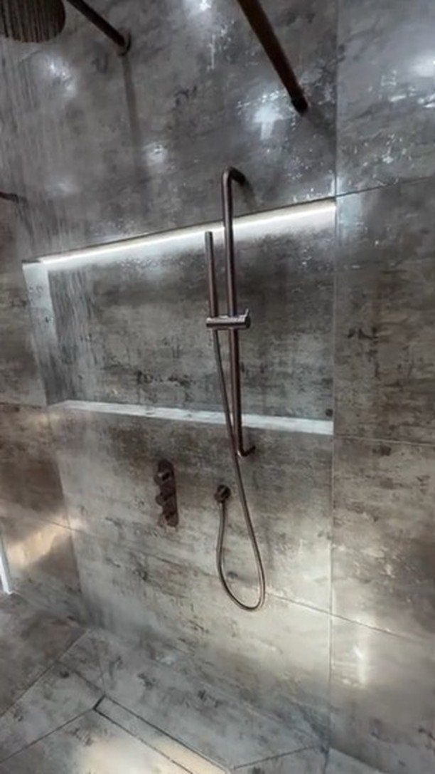 Grey stone tiled shower with a lit recessed niche and dark metal fixtures