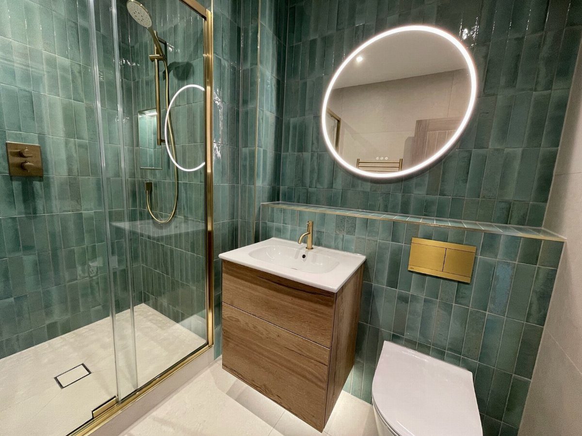 Modern bathroom with teal tiles, wooden vanity, and gold shower fixtures.