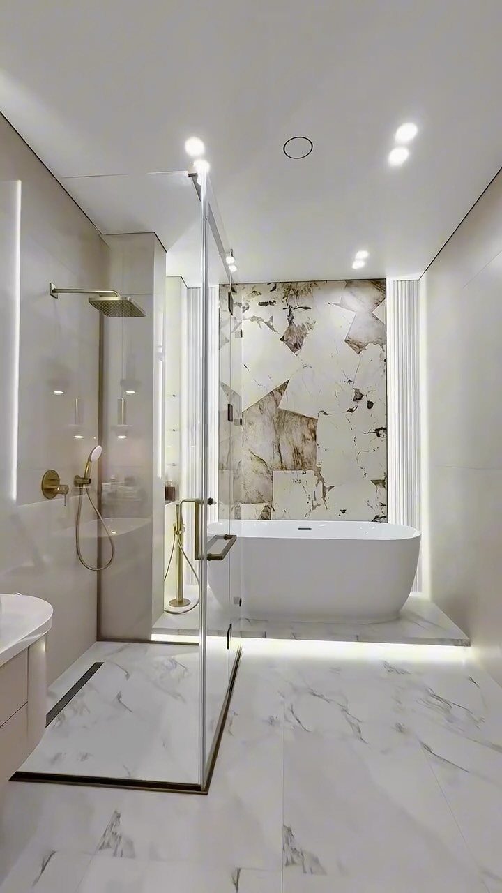 Modern bathroom with white marble surfaces, gold fixtures, and a freestanding bathtub.