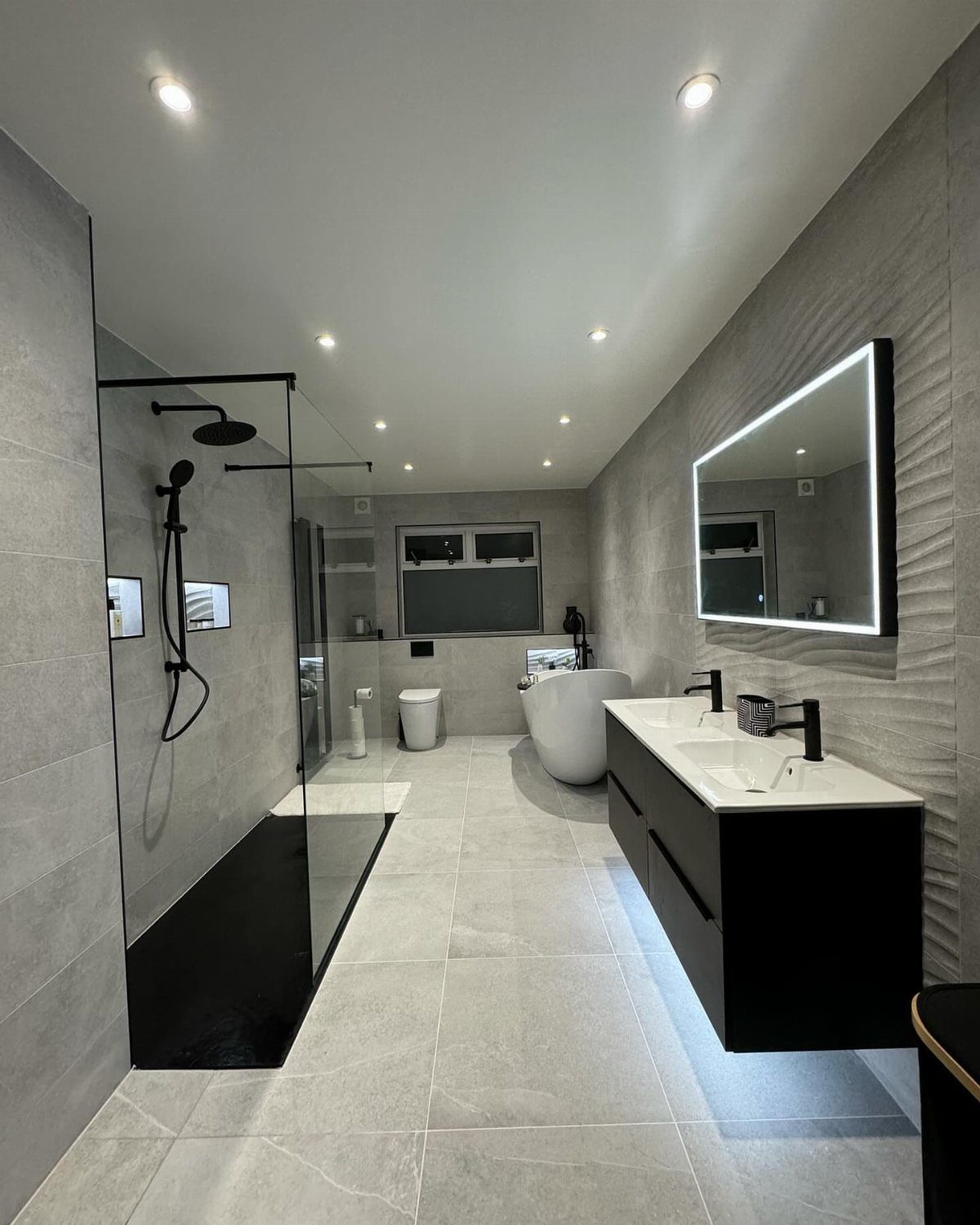 Modern bathroom featuring a white freestanding bathtub, black floating vanity, and glass shower.