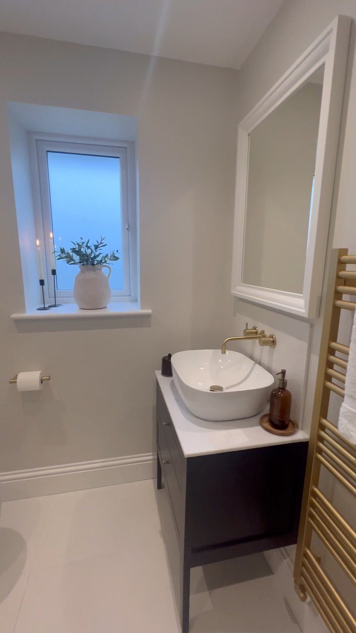 Modern bathroom with dark blue vanity, white vessel sink, and gold towel rail.
