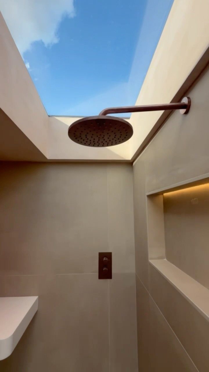 Copper rain shower head under an open ceiling showing a blue sky