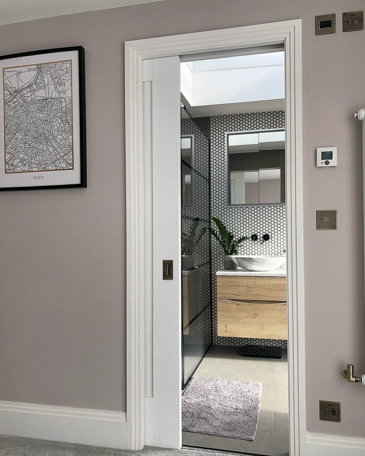 White pocket door opening into a modern bathroom with wooden vanity and mosaic tiles.