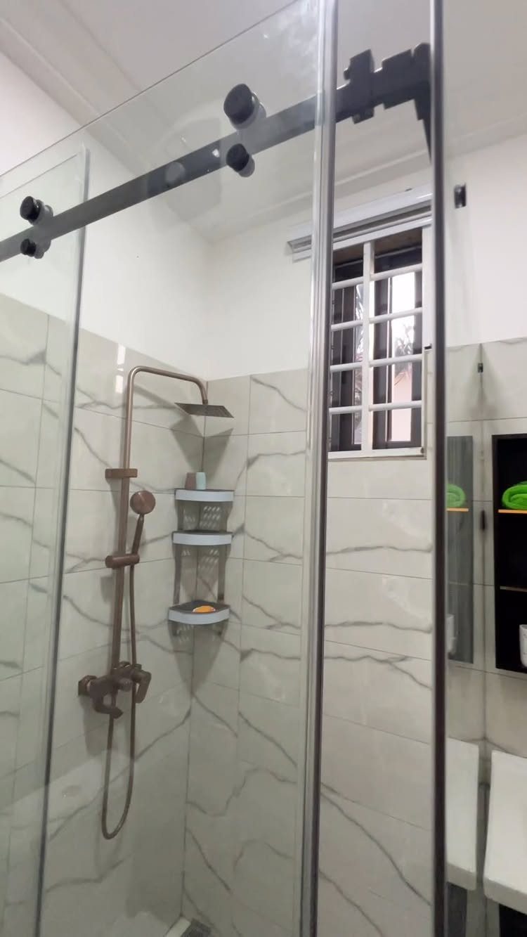 Glass shower enclosure with black sliding doors and white marble wall tiles.