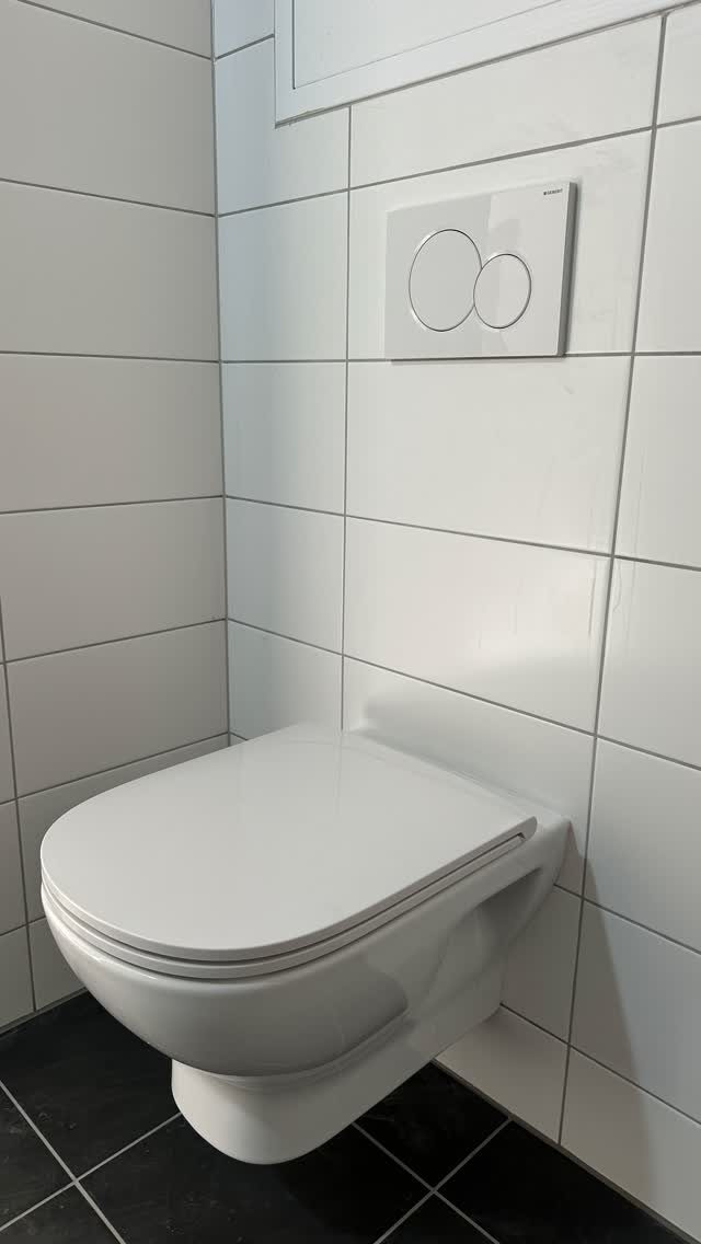 Wall-hung white toilet installed against white tiled walls with black floor tiles.