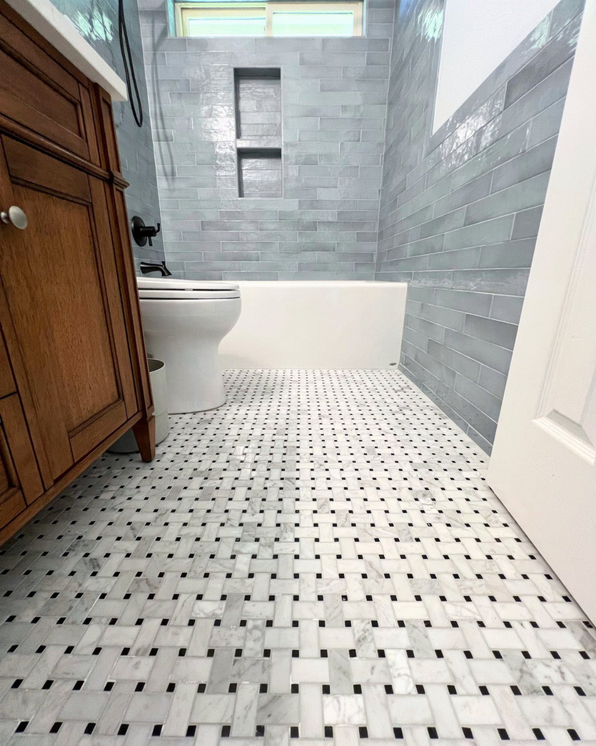 Basketweave marble floor tiles in a small bathroom with grey wall tiles.