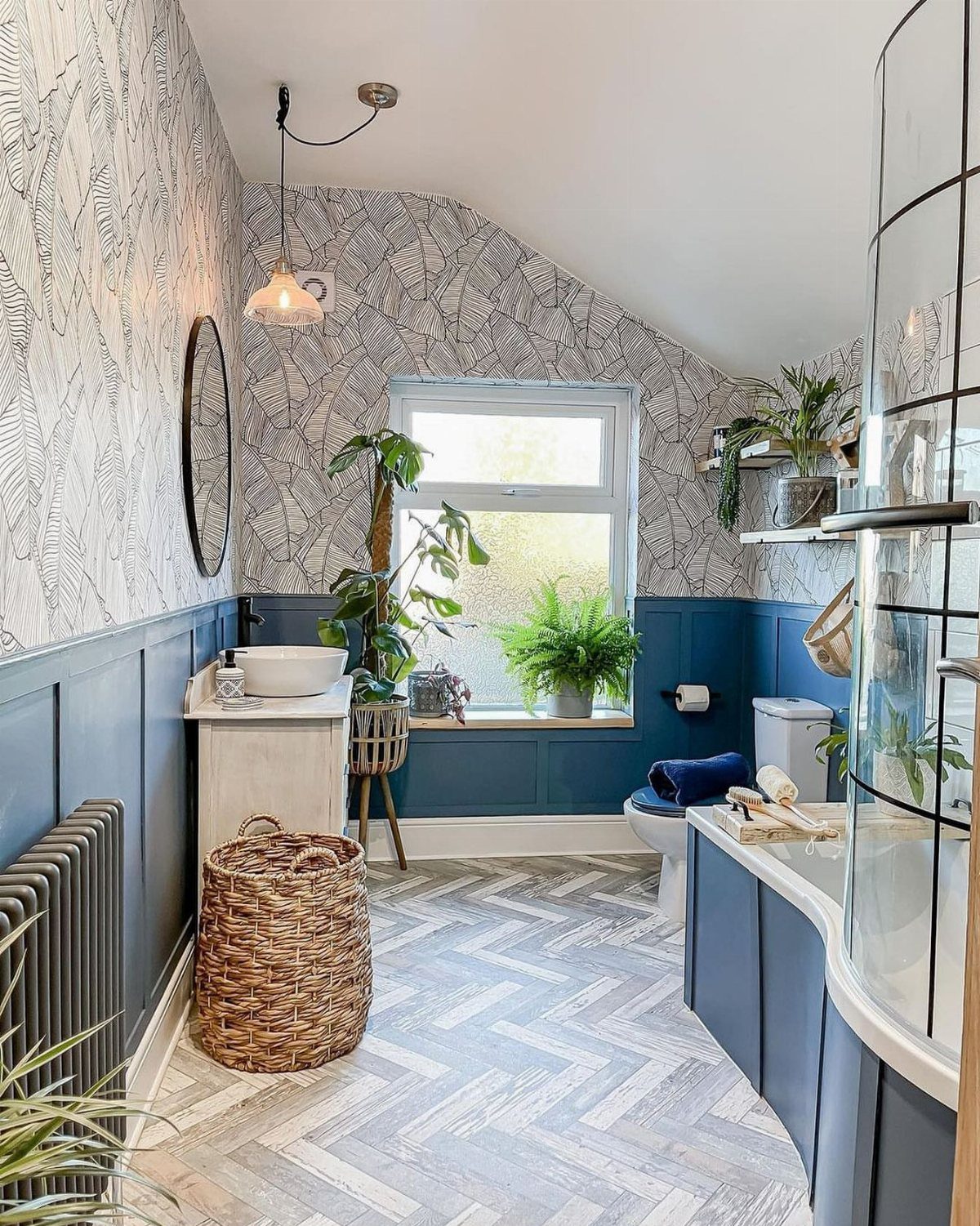 Herringbone patterned floor tiles in a small bathroom with blue walls and plants