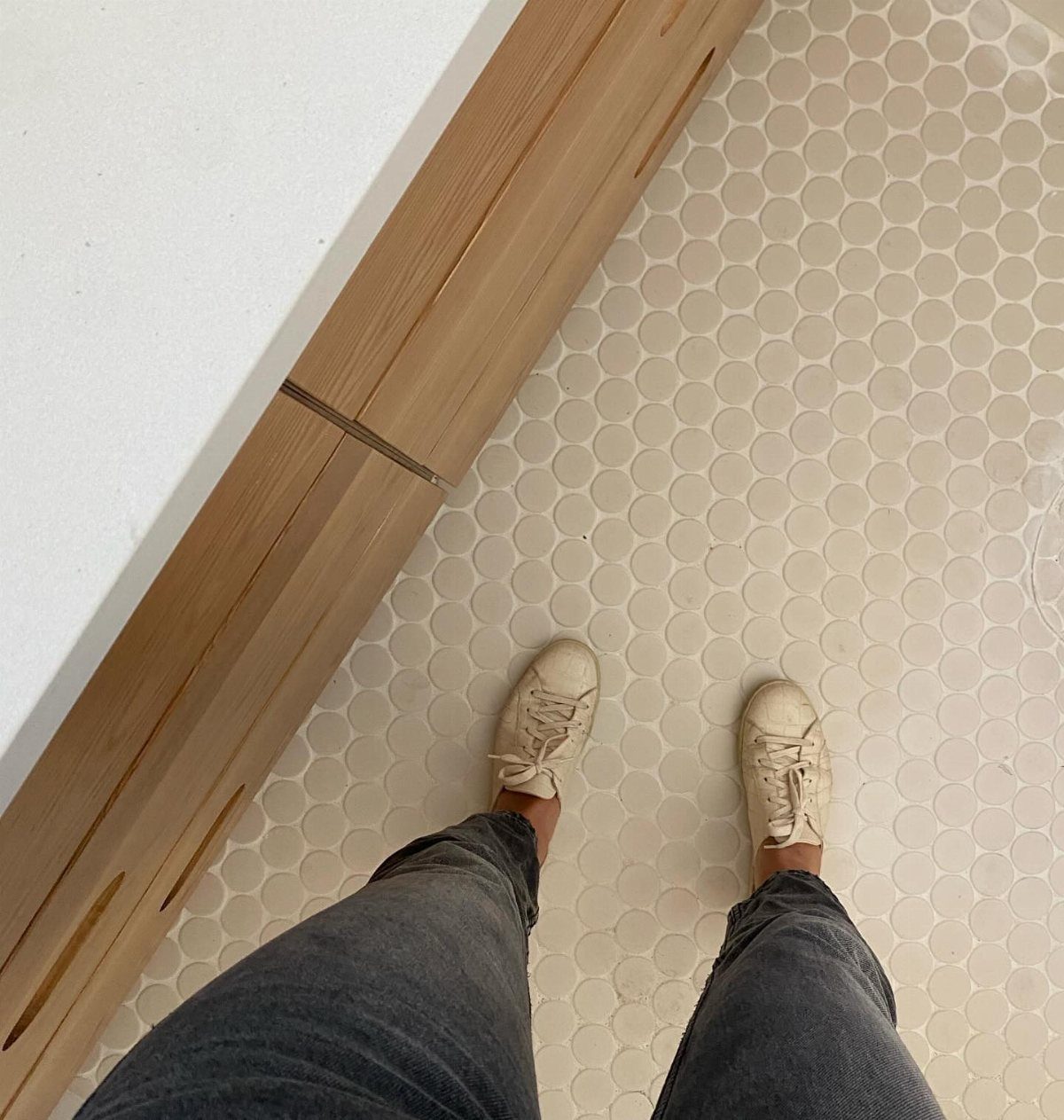 Small off-white penny round floor tiles next to a light wood baseboard.