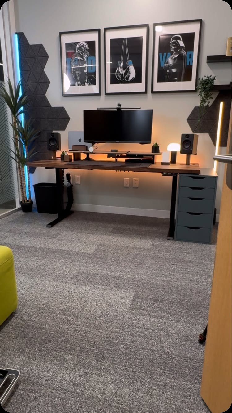 Gaming desk setup with monitor, framed posters, and hexagonal wall panels in a room.
