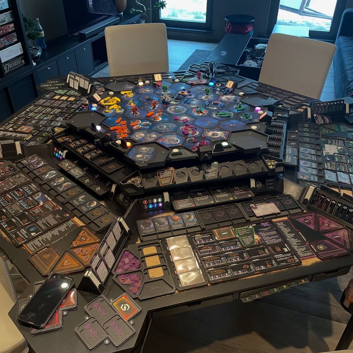 Hexagonal black gaming table with integrated LEDs and complex board game components