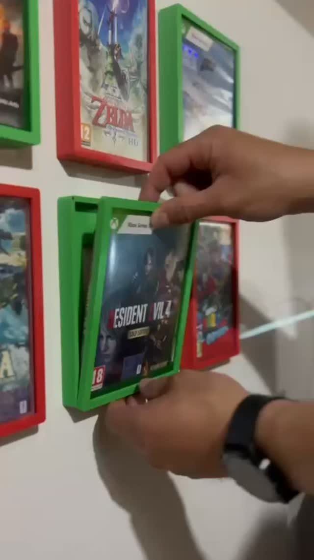 Hands inserting a video game case into a green wall-mounted storage holder.
