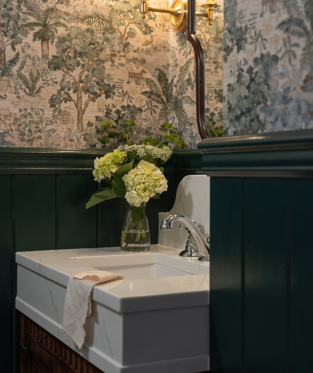 White marble sink and dark green walls with botanical landscape wallpaper and flowers